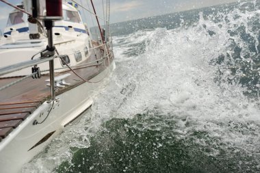 Fırtınada açık denizde yelken açan eski klasik bir yat. Tahta meşe güvertesi. Direğe ve yelkenlere bakın. Ketçap yelkenli. Dalgalar, su sıçramaları. Gezi, tatil, yelkenli yarışı, spor, boş zaman aktivitesi.