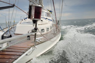 Fırtınada açık denizde yelken açan eski klasik bir yat. Tahta meşe güvertesi. Direğe ve yelkenlere bakın. Ketçap yelkenli. Dalgalar, su sıçramaları. Gezi, tatil, yelkenli yarışı, spor, boş zaman aktivitesi.