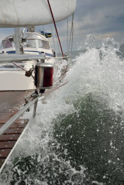 Fırtınada açık denizde yelken açan eski klasik bir yat. Tahta meşe güvertesi. Direğe ve yelkenlere bakın. Ketçap yelkenli. Dalgalar, su sıçramaları. Gezi, tatil, yelkenli yarışı, spor, boş zaman aktivitesi.
