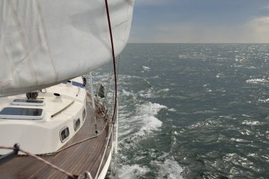 Fırtınada açık denizde yelken açan eski klasik bir yat. Tahta meşe güvertesi. Direğe ve yelkenlere bakın. Ketçap yelkenli. Dalgalar, su sıçramaları. Gezi, tatil, yelkenli yarışı, spor, boş zaman aktivitesi.