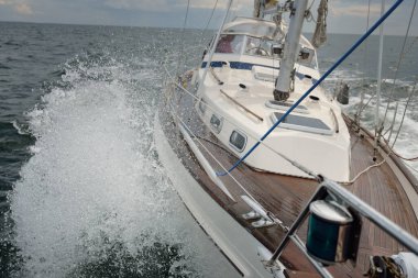 Fırtınada açık denizde yelken açan eski klasik bir yat. Tahta meşe güvertesi. Direğe ve yelkenlere bakın. Ketçap yelkenli. Dalgalar, su sıçramaları. Gezi, tatil, yelkenli yarışı, spor, boş zaman aktivitesi.