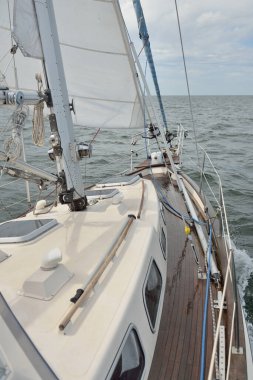 Fırtınada açık denizde yelken açan eski klasik bir yat. Tahta meşe güvertesi. Direğe ve yelkenlere bakın. Ketçap yelkenli. Dalgalar, su sıçramaları. Gezi, tatil, yelkenli yarışı, spor, boş zaman aktivitesi.