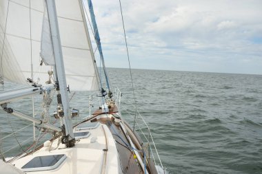 Fırtınada açık denizde yelken açan eski klasik bir yat. Tahta meşe güvertesi. Direğe ve yelkenlere bakın. Ketçap yelkenli. Dalgalar, su sıçramaları. Gezi, tatil, yelkenli yarışı, spor, boş zaman aktivitesi.