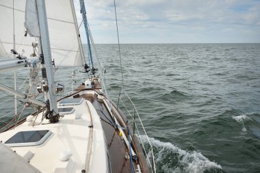 Fırtınada açık denizde yelken açan eski klasik bir yat. Tahta meşe güvertesi. Direğe ve yelkenlere bakın. Ketçap yelkenli. Dalgalar, su sıçramaları. Gezi, tatil, yelkenli yarışı, spor, boş zaman aktivitesi.