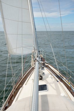 Fırtınada açık denizde yelken açan eski klasik bir yat. Tahta meşe güvertesi. Direğe ve yelkenlere bakın. Ketçap yelkenli. Dalgalar, su sıçramaları. Gezi, tatil, yelkenli yarışı, spor, boş zaman aktivitesi.