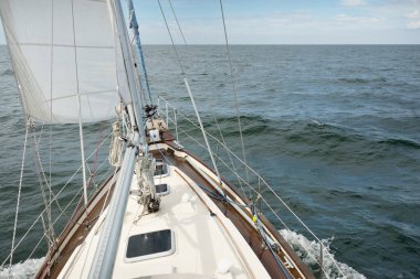 Fırtınada açık denizde yelken açan eski klasik bir yat. Tahta meşe güvertesi. Direğe ve yelkenlere bakın. Ketçap yelkenli. Dalgalar, su sıçramaları. Gezi, tatil, yelkenli yarışı, spor, boş zaman aktivitesi.