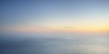 Kalın beyaz sis bulutları içinde nefes kesici panoramik deniz manzarası. Parlak gökyüzü, gece yarısı güneşi, alacakaranlık. Resimli bir manzara var. Rüya gibi bir manzara. Saf doğa, çevre, ekoloji, turizm