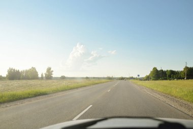 Tarımsal alan ve ormanın içinden geçen ülke otoyolu. Fırtınadan sonra dramatik bir gökyüzü. Yazın kırsal alanda. Yumuşak güneş ışığı. Tatiller, yol gezisi, sürüş, yolculuk