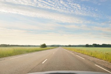 Gündoğumunda tarla ve ormanın içinden (asfalt yol) geçer. Yumuşak güneş ışığı, parlayan bulutlar. Tatiller, lojistik, ücra yerler. Arabadan bak.