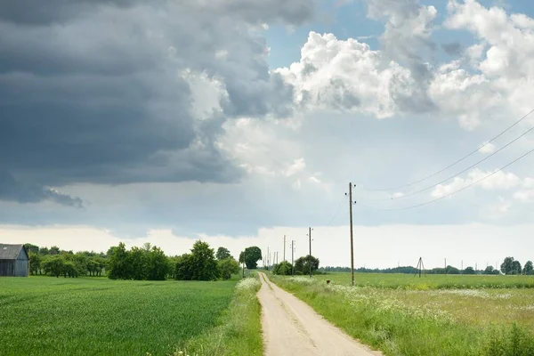 Fırtınadan sonra tarladan geçen boş köy yolu. Arabadan bir manzara. Idyllic kırsal kesim. Renkli, parlayan günbatımı bulutları. Ulaşım, yolculuk, özgürlük, seyahat tutkusu, uzak yerler kavramları.