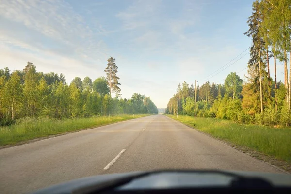 Gündoğumunda tarla ve ormanın içinden (asfalt yol) geçer. Yumuşak güneş ışığı, parlayan bulutlar. Tatiller, lojistik, ücra yerler. Arabadan bak.