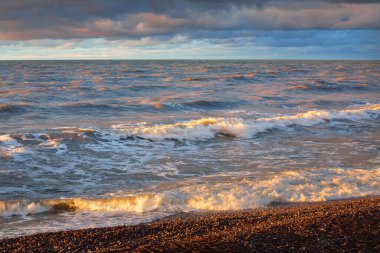 Gün batımında Baltık kıyısı. Yumuşak altın güneş ışığı, dramatik gökyüzü, parlayan bulutlar, dalgalar. Idyllic deniz manzarası. Liepaja, Letonya. Seyahat yerleri, eko-turizm, doğa. Resimli panoramik manzara