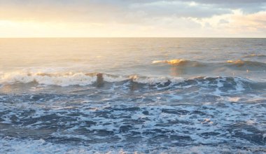 Gün batımında Baltık kıyısı. Yumuşak altın güneş ışığı, dramatik gökyüzü, parlayan bulutlar, dalgalar. Idyllic deniz manzarası. Seyahat yerleri, eko-turizm, doğa, hava durumu, iklim değişikliği. Resimli panoramik manzara