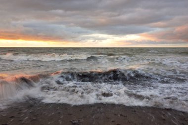 Gün batımında Baltık kıyısı. Yumuşak altın güneş ışığı, dramatik gökyüzü, parlayan bulutlar, dalgalar. Idyllic deniz manzarası. Liepaja, Letonya. Seyahat yerleri, eko-turizm, doğa. Resimli panoramik manzara