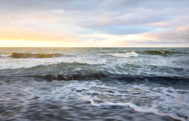Gün batımında Baltık kıyısı. Yumuşak altın güneş ışığı, dramatik gökyüzü, parlayan bulutlar, dalgalar. Idyllic deniz manzarası. Seyahat yerleri, eko-turizm, doğa, hava durumu, iklim değişikliği. Resimli panoramik manzara