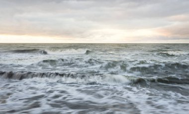 Gün batımında Baltık kıyısı. Yumuşak altın güneş ışığı, dramatik gökyüzü, parlayan bulutlar, dalgalar. Idyllic deniz manzarası. Seyahat yerleri, eko-turizm, doğa, hava durumu, iklim değişikliği. Resimli panoramik manzara