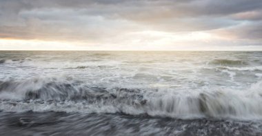 Gün batımında Baltık kıyısı. Yumuşak altın güneş ışığı, dramatik gökyüzü, parlayan bulutlar, dalgalar. Idyllic deniz manzarası. Seyahat yerleri, eko-turizm, doğa, hava durumu, iklim değişikliği. Resimli panoramik manzara