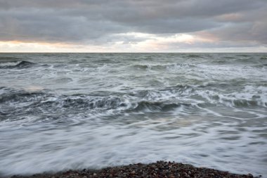 Gün batımında Baltık kıyısı. Yumuşak altın güneş ışığı, dramatik gökyüzü, parlayan bulutlar, dalgalar. Idyllic deniz manzarası. Liepaja, Letonya. Seyahat yerleri, eko-turizm, doğa. Resimli panoramik manzara