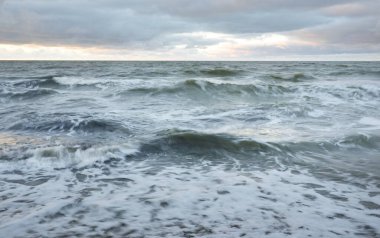 Gün batımında Baltık kıyısı. Yumuşak altın güneş ışığı, dramatik gökyüzü, parlayan bulutlar, dalgalar. Idyllic deniz manzarası. Seyahat yerleri, eko-turizm, doğa, hava durumu, iklim değişikliği. Resimli panoramik manzara