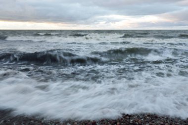 Gün batımında Baltık kıyısı. Yumuşak altın güneş ışığı, dramatik gökyüzü, parlayan bulutlar, dalgalar. Idyllic deniz manzarası. Liepaja, Letonya. Seyahat yerleri, eko-turizm, doğa. Resimli panoramik manzara