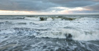Gün batımında Baltık kıyısı. Yumuşak altın güneş ışığı, dramatik gökyüzü, parlayan bulutlar, dalgalar. Idyllic deniz manzarası. Seyahat yerleri, eko-turizm, doğa, hava durumu, iklim değişikliği. Resimli panoramik manzara