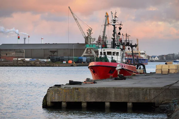 General cargo ship and fishing boat anchored in a trading port. Cranes in the background. Liepaja, Latvia, Baltic sea. Freight transportation, logistics, global communications, industry, economy