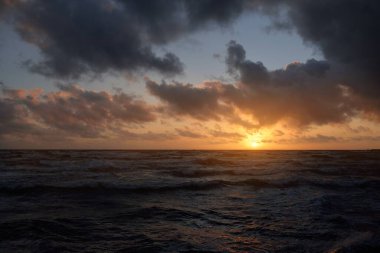 Fırtınadan sonra parlayan pembe ve altın rengi günbatımı bulutlarıyla mavi gökyüzünün altında Baltık Denizi kıyısında. Dalgalar çarpıyor. Doğa, çevre koruma, eko-turizm. Resimli panoramik manzara