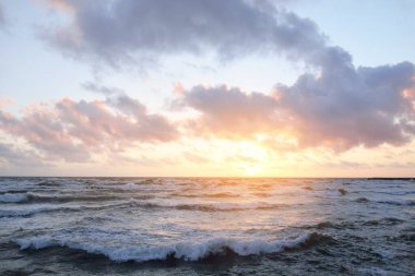 Fırtınadan sonra parlayan günbatımı bulutlarıyla mavi gökyüzünün altında Baltık Denizi kıyısında. Su yüzeyi dokusu, çarpan dalgalar. Doğa, çevre koruma, eko-turizm. Resimli panoramik manzara