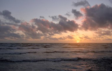 Fırtınadan sonra parlayan günbatımı bulutlarıyla mavi gökyüzünün altında Baltık Denizi kıyısında. Su yüzeyi dokusu, çarpan dalgalar. Doğa, çevre koruma, eko-turizm. Resimli panoramik manzara