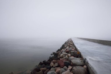 Kumlu sahilden Baltık Denizi 'nin panoramik manzarası. Deniz fenerine dolaş, dalgalar. Kalın beyaz sis, sis. Dalgalar, su sıçramaları, uzun pozlama. Deniz Burnu. Resimli monokrom manzarası