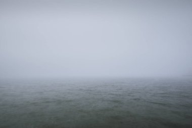 Kumlu sahilden Baltık Denizi 'nin panoramik manzarası. Kalın beyaz sis, sis. Dalgalar, su sıçramaları. Deniz Burnu. Hava, iklim değişikliği, doğa, tehlike, gemi enkazı kavramları. Resimli monokrom manzarası