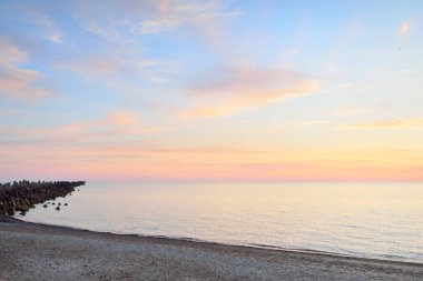 Mavi gökyüzünün altında, parlak pembe ve altın renkli günbatımı bulutlarıyla Baltık deniz kıyısında. Kaya kıyısı, dalgalar. Idyllic deniz manzarası. - Letonya. Doğa, çevre koruma, eko-turizm. Resim gibi bir manzara.