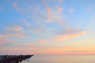 Mavi gökyüzünün altında, parlak pembe ve altın renkli günbatımı bulutlarıyla Baltık deniz kıyısında. Kaya kıyısı, dalgalar. Idyllic deniz manzarası. - Letonya. Doğa, çevre koruma, eko-turizm. Resim gibi bir manzara.