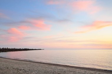 Mavi gökyüzünün altında, parlak pembe ve altın renkli günbatımı bulutlarıyla Baltık deniz kıyısında. Kaya kıyısı, dalgalar. Idyllic deniz manzarası. - Letonya. Doğa, çevre koruma, eko-turizm. Resim gibi bir manzara.