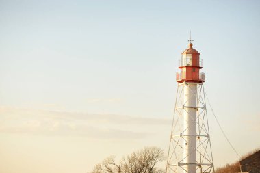Deniz fenerine karşı açık mavi gün batımı gökyüzü. Hafif ışık, altın saat. Letonya 'nın Pape köyü. Idyllic manzara. İnşaat, sahil güvenlik, yön bulma, umut ve barışın sembolü. Panoramik görünüm, boşluğu kopyala