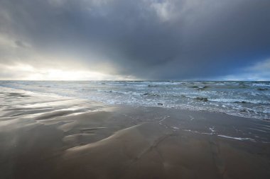 Kumlu bir sahilden (kum tepeleri) Baltık denizinin panoramik görüntüsü. Koyu bulutlu dramatik bir gökyüzü. Dalgalar, su sıçramaları. Idyllic deniz manzarası. Sıcak kış havası, iklim değişikliği, doğa. Danimarka