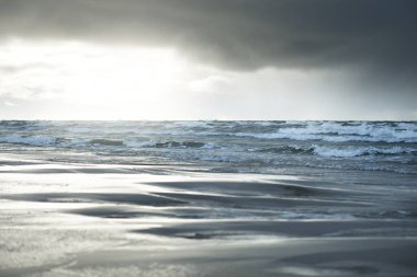 Kumlu bir sahilden (kum tepeleri) Baltık denizinin panoramik görüntüsü. Koyu bulutlu dramatik bir gökyüzü. Dalgalar, su sıçramaları. Idyllic deniz manzarası. Sıcak kış havası, iklim değişikliği, doğa. Danimarka