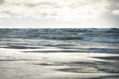 Kumlu bir sahilden (kum tepeleri) Baltık denizinin panoramik görüntüsü. Koyu bulutlu dramatik bir gökyüzü. Dalgalar, su sıçramaları. Idyllic deniz manzarası. Sıcak kış havası, iklim değişikliği, doğa. Danimarka