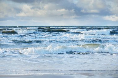 Kumlu sahilden Baltık denizinin panoramik görüntüsü (kum tepeleri). Parlayan bulutları, güneş ışınları olan dramatik bir gökyüzü. Dalgalar, su sıçramaları. Idyllic deniz manzarası. Sıcak kış havası, iklim değişikliği, doğa. Danimarka