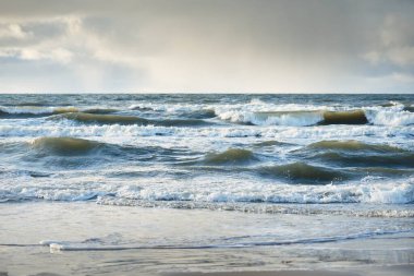 Kumlu sahilden Baltık denizinin panoramik görüntüsü (kum tepeleri). Parlayan bulutları, güneş ışınları olan dramatik bir gökyüzü. Dalgalar, su sıçramaları. Idyllic deniz manzarası. Sıcak kış havası, iklim değişikliği, doğa. Danimarka