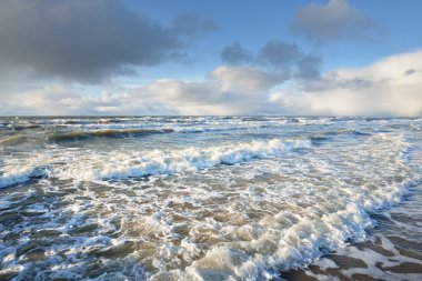 Kumlu sahilden Baltık denizinin panoramik görüntüsü (kum tepeleri). Parlayan bulutları, güneş ışınları olan dramatik bir gökyüzü. Dalgalar, su sıçramaları. Idyllic deniz manzarası. Sıcak kış havası, iklim değişikliği, doğa. Danimarka