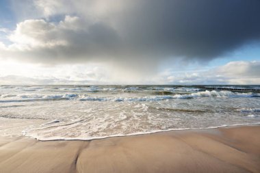 Kumlu sahilden Baltık denizinin panoramik görüntüsü (kum tepeleri). Parlayan bulutları, güneş ışınları olan dramatik bir gökyüzü. Dalgalar, su sıçramaları. Idyllic deniz manzarası. Sıcak kış havası, iklim değişikliği, doğa. Danimarka