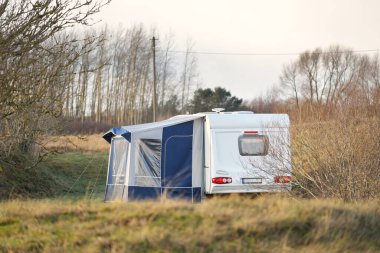 Karavan karavanı, açık bir bahar gününde küçük bir köyün yeşil çimenliğine park etmiş. Normandiya, Fransa. Ulaşım, karavan, karavan, yol gezisi, yerel seyahat, eko-turizm, dinlenme, boş zaman aktivitesi