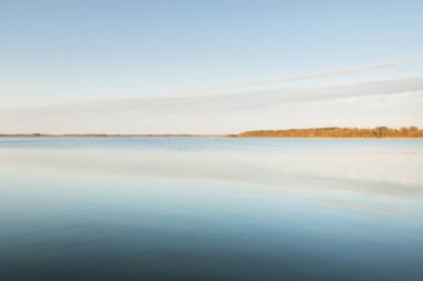 Gün batımında mavi orman gölü (nehir) panoramik hava manzarası. Yumuşak güneş ışığı, berrak gökyüzü, suya yansıyan yansımalar. Baharın başında. İdealist pastoral manzara. Doğa, çevre, ekoloji, eko-turizm