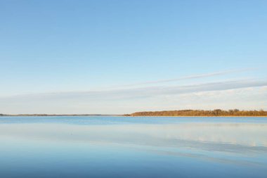 Gün batımında mavi orman gölü (nehir) panoramik hava manzarası. Yumuşak güneş ışığı, berrak gökyüzü, suya yansıyan yansımalar. Baharın başında. İdealist pastoral manzara. Doğa, çevre, ekoloji, eko-turizm