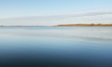 Gün batımında mavi orman gölü (nehir) panoramik hava manzarası. Yumuşak güneş ışığı, berrak gökyüzü, suya yansıyan yansımalar. Baharın başında. İdealist pastoral manzara. Doğa, çevre, ekoloji, eko-turizm