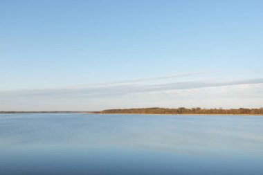 Gün batımında mavi orman gölü (nehir) panoramik hava manzarası. Yumuşak güneş ışığı, berrak gökyüzü, suya yansıyan yansımalar. Baharın başında. İdealist pastoral manzara. Doğa, çevre, ekoloji, eko-turizm