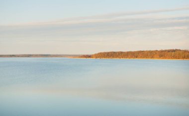 Gün batımında mavi orman gölü (nehir) panoramik hava manzarası. Yumuşak güneş ışığı, berrak gökyüzü, suya yansıyan yansımalar. Baharın başında. İdealist pastoral manzara. Doğa, çevre, ekoloji, eko-turizm