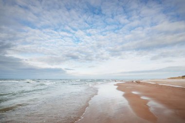 Kumlu bir sahilden (kum tepeleri) Baltık denizinin panoramik görüntüsü. Parlayan bulutlar, dalgalar ve su sıçramalarıyla dramatik bir gökyüzü. Idyllic deniz manzarası. Sıcak kış havası, iklim değişikliği, doğa. Danimarka