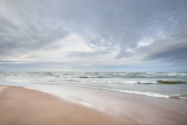 Kumlu bir sahilden (kum tepeleri) Baltık denizinin panoramik görüntüsü. Parlayan bulutlar, dalgalar ve su sıçramalarıyla dramatik bir gökyüzü. Idyllic deniz manzarası. Sıcak kış havası, iklim değişikliği, doğa. Danimarka